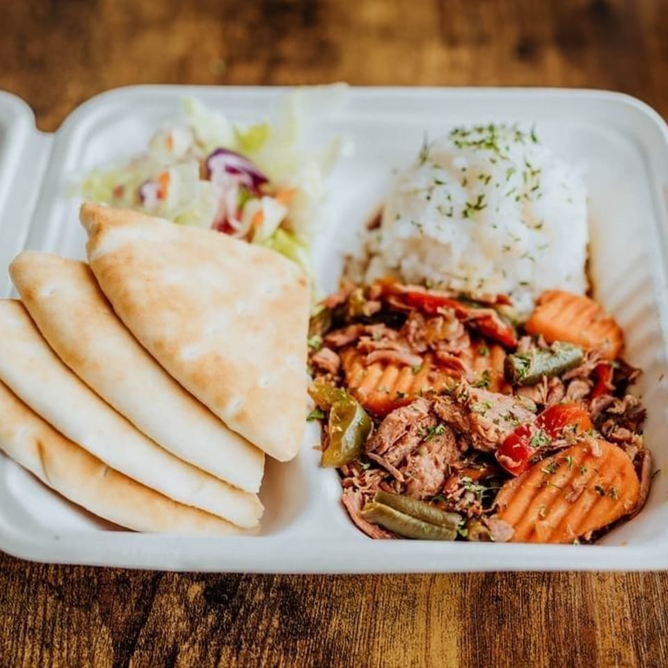 Takeaway tray with shredded meat, vegetables, white rice, flatbread, and slaw on a wooden table.